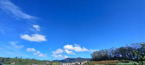 a blue sky with clouds and trees on a hill at Moonplain Bungalows in Nuwara Eliya