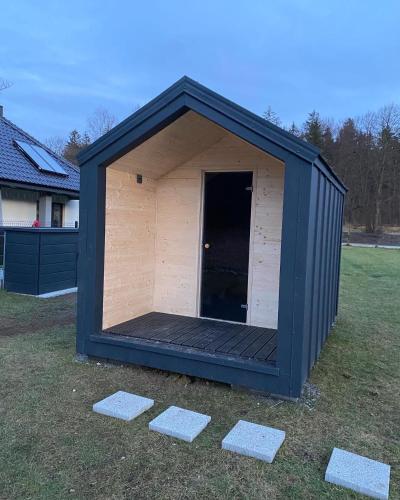 a large black shed with a door in the grass at Holiday Hill Karpnki, Sauna, Domek Hygge-balia, Domek Lagom-jacuzzi in Karpniki