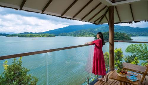 a woman in a red dress standing on a balcony overlooking a lake at MOUNTAIN SHADOWS RESORT Wayanad in Wayanad
