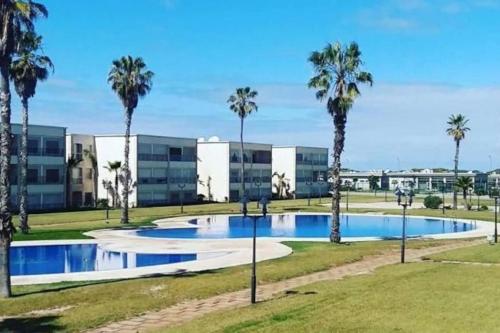 a swimming pool with palm trees in front of a building at Ola Blanca Sidi rahal Apparthotel in Sidi Rahal