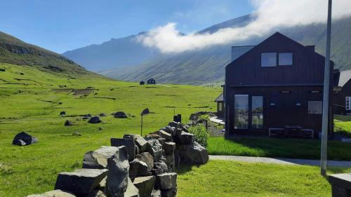 a house in a field with a rock wall at Okkara summarhús við Gjógv - Luxury cottage - Unique location in Við Gjógv