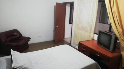 - une chambre avec un lit, une télévision et une chaise dans l'établissement La Casa de Lu Los Rosales, à Manizales