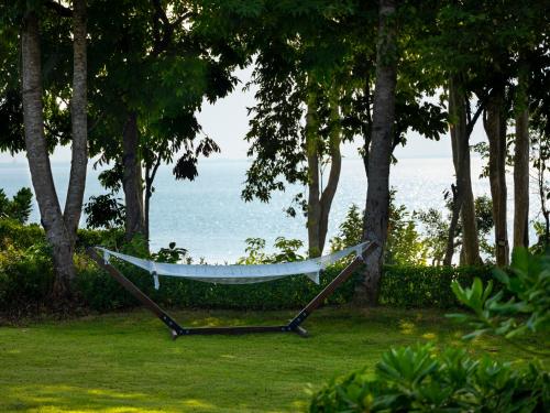 a hammock in a yard with trees and the ocean at The ShellSea Krabi I Luxury Beach Front Resort & Pool Villa in Ao Nam Mao