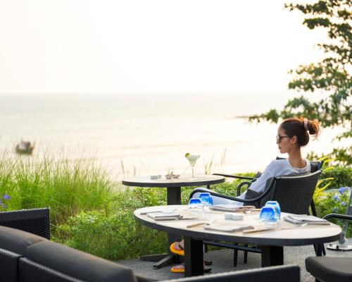 a woman sitting at a table by the beach at The ShellSea Krabi I Luxury Beach Front Resort & Pool Villa in Ao Nam Mao