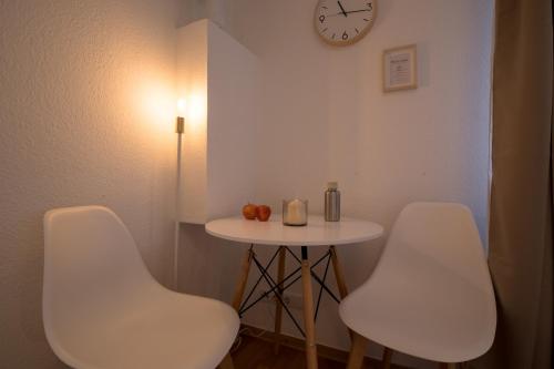 twee witte stoelen en een tafel met een klok aan de muur bij Modernes & zentrales Micro-Apartment in Boppard
