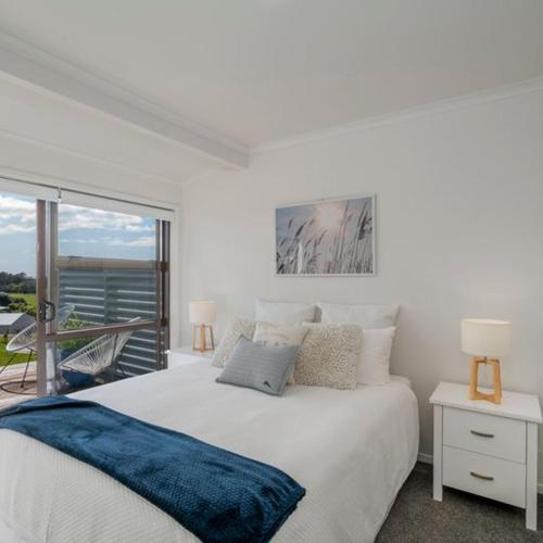 Un dormitorio blanco con una cama grande y un balcón. en Hahei Beach Dolphin cottage, en Hahei