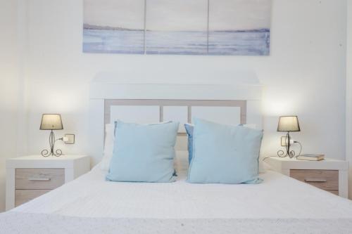 a white bedroom with a bed with blue pillows at La Barrosa con vistas al mar in Novo Sancti Petri
