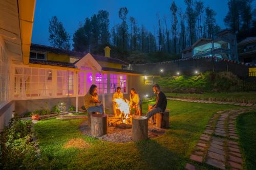 um grupo de pessoas sentadas em torno de um incêndio em um quintal em The Hosteller Ooty em Ooty