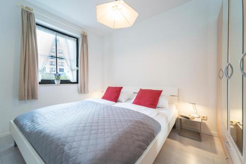 een witte slaapkamer met een groot bed met rode kussens bij Haus Titania Wohnung 1 in Grömitz