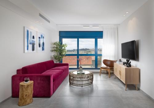 AMALON Boutique Apartments في القدس: غرفة معيشة مع أريكة حمراء وتلفزيون