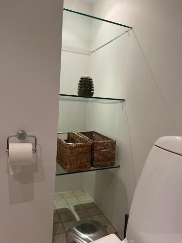 a bathroom with a toilet with a glass shelf and baskets at Farmens Gæstehus in Svebølle