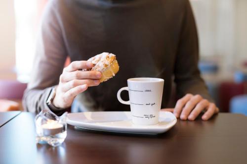 a person eating a donut next to a cup of coffee at Motel L Lund in Lund