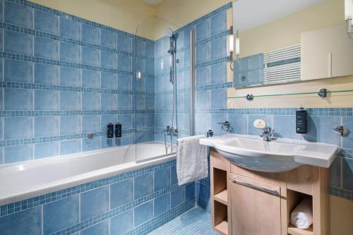 プラハにあるマメゾン レジデンス ベルギツカ プラハの青いタイル張りのバスルーム(シンク、バスタブ付)