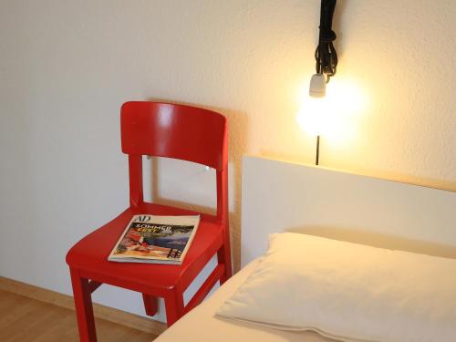 uma cadeira vermelha sentada ao lado de uma cama com uma revista em apartment-S Sonnenrain em Lörrach