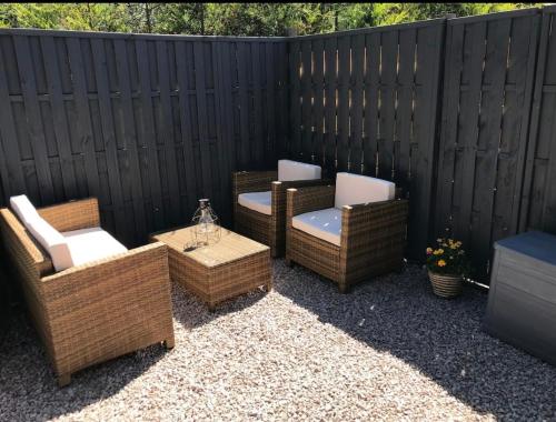 a patio with wicker chairs and tables and a fence at Riverside Hideaway in Kincraig