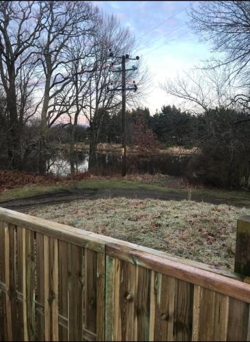 a yard with a wooden fence and a field at Riverside Hideaway in Kincraig