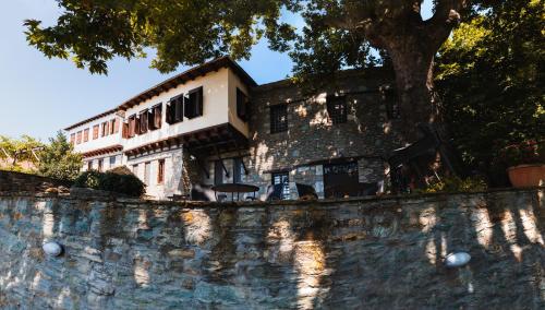 a building behind a stone wall with a tree at Palio Eleotrivio Guesthouse in Agios Lavrentios