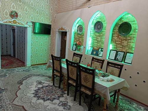ein Esszimmer mit einem Tisch, Stühlen und Fenstern in der Unterkunft Khiva Ibrohim Guest House in Xiva
