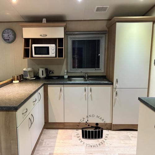 a kitchen with white cabinets and a microwave at Bianca and marks 8 berth Caravan with Hot tub in Tattershall