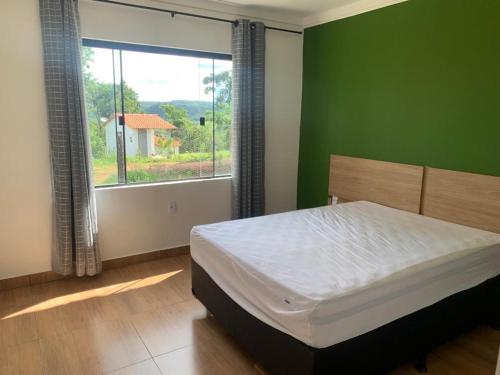 um quarto com uma cama com uma parede verde e uma janela em Charme Corumbá em Alexânia