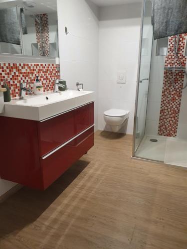 La salle de bains est pourvue d'un lavabo rouge et de toilettes. dans l'établissement L'Obernois situé dans 1 résidence privée, à Obernai