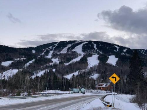a road with a snow covered mountain in the background at Appartement Mont Édouard, Hébergement paisible à la montagne in LʼAnse-Saint-Jean