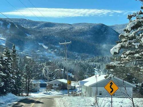 a snow covered mountain with a house and a sign at Appartement Mont Édouard, Hébergement paisible à la montagne in LʼAnse-Saint-Jean