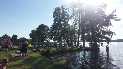 a group of people sitting on the grass by the water at Biały Żagiel - Dom do wynajęcia Pluski in Pluski
