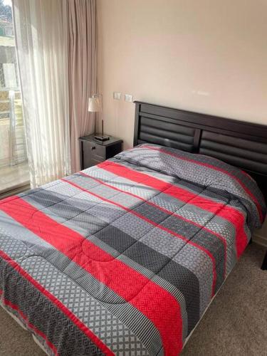 een slaapkamer met een bed met een rode en grijze deken bij Departamento Centro Viña Playa in Viña del Mar