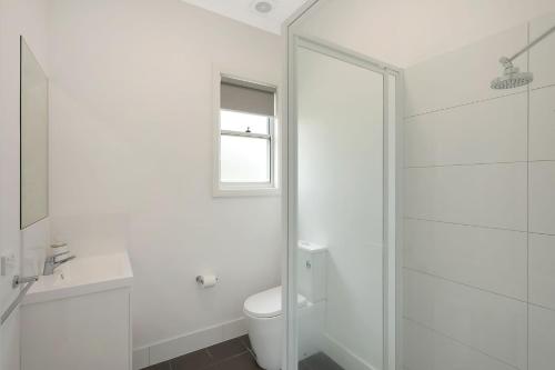 a white bathroom with a toilet and a glass shower at Henkley Cottage 1 Isaiah in Central Tilba