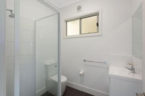 a white bathroom with a toilet and a window at Henkley Cottage 2 Jeremiah in Central Tilba