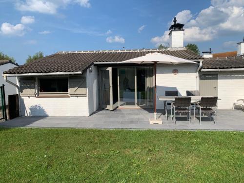 een wit huis met een patio met stoelen en een parasol bij Groendijk 105 in Koksijde