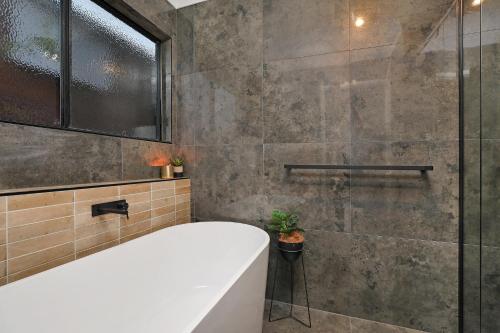 a bathroom with a tub and a glass shower at Luxury Holiday Home in Alex - Heated Pool - Pets Allowed in Alexandra Headland