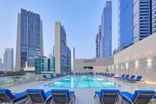 a swimming pool with chairs and a city skyline at Rose Rayhaan by Rotana - Dubai in Dubai