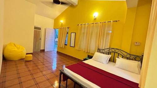 a bedroom with a bed and a yellow wall at Muffys Guest House in Arpora