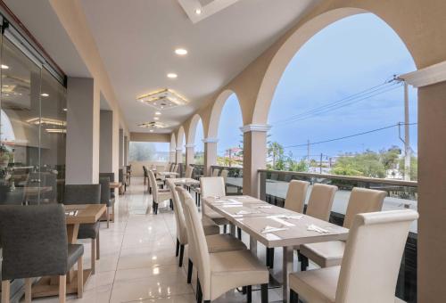 a restaurant with white tables and chairs and windows at Karras Grande Resort in Tsilivi