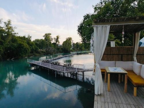 a patio with a table and a bridge over a body of water at Şelale Park Gizli Bahçe Glamping in Viransenir