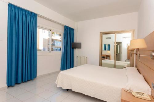 a bedroom with a bed and a window with blue curtains at Hotel Ibiza Playa in Ibiza Town