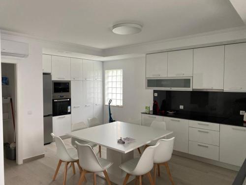 a white kitchen with a white table and chairs at Torrezinha- Moradia Moderna em condomínio com piscina in Salir de Porto