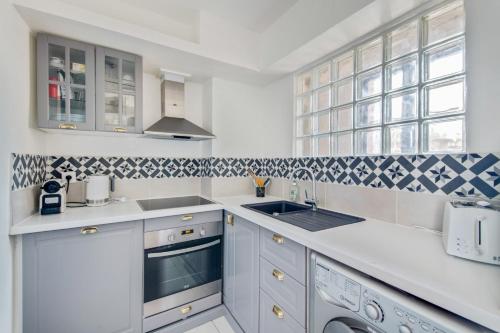 une cuisine avec des armoires blanches, un évier et une fenêtre dans l'établissement Le Milady- Versailles, à Versailles