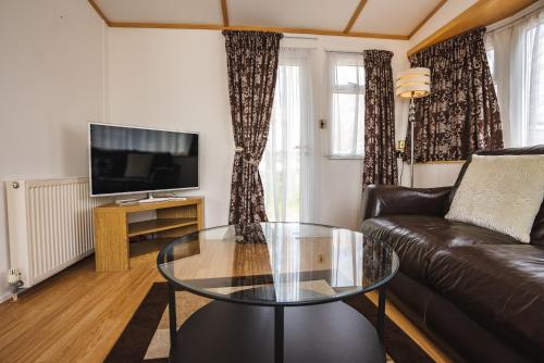 a living room with a leather couch and a glass table at Lochlands 2br family caravan - pets-play park in Forfar