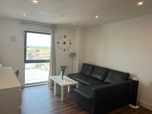 a living room with a black couch and a clock on the wall at Lovely luxury 1-Bed Apartment in Wembley in London