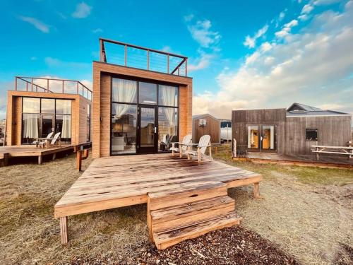 una casa con una terraza de madera en un campo en Basecamp Tiny House Eco Resort en IJmuiden