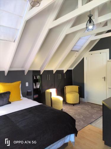a bedroom with a bed and two yellow chairs at Rozenhof Guest Cottages in George