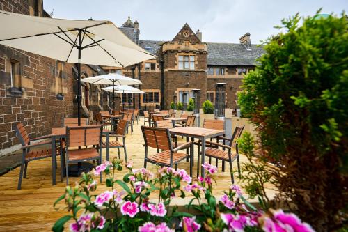 un patio con tavoli, sedie e fiori rosa di Stirling Highland Hotel- Part of the Cairn Collection a Stirling