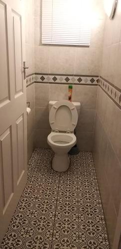 a bathroom with a toilet and a tile floor at Rose Holiday Home in Durban