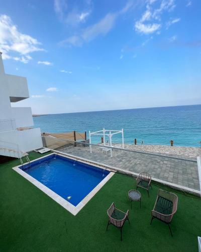 a pool with chairs and the ocean in the background at Wadi Shab Beach Villa in Sur