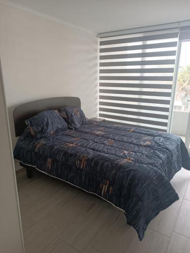 a bed with a blue comforter in a room with a window at DEPARTAMENTO EN LA SERENA in La Serena