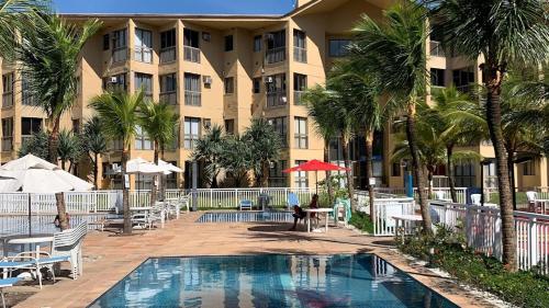 a resort with a pool and palm trees and a building at Reserva do Sahy-Mangaratiba Condado Loft Sol & Sal in Mangaratiba