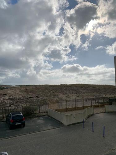 un coche aparcado en un estacionamiento junto a una valla en Agréable T2 Lacanau Ocean bord de mer. Expo sud. en Lacanau-Océan